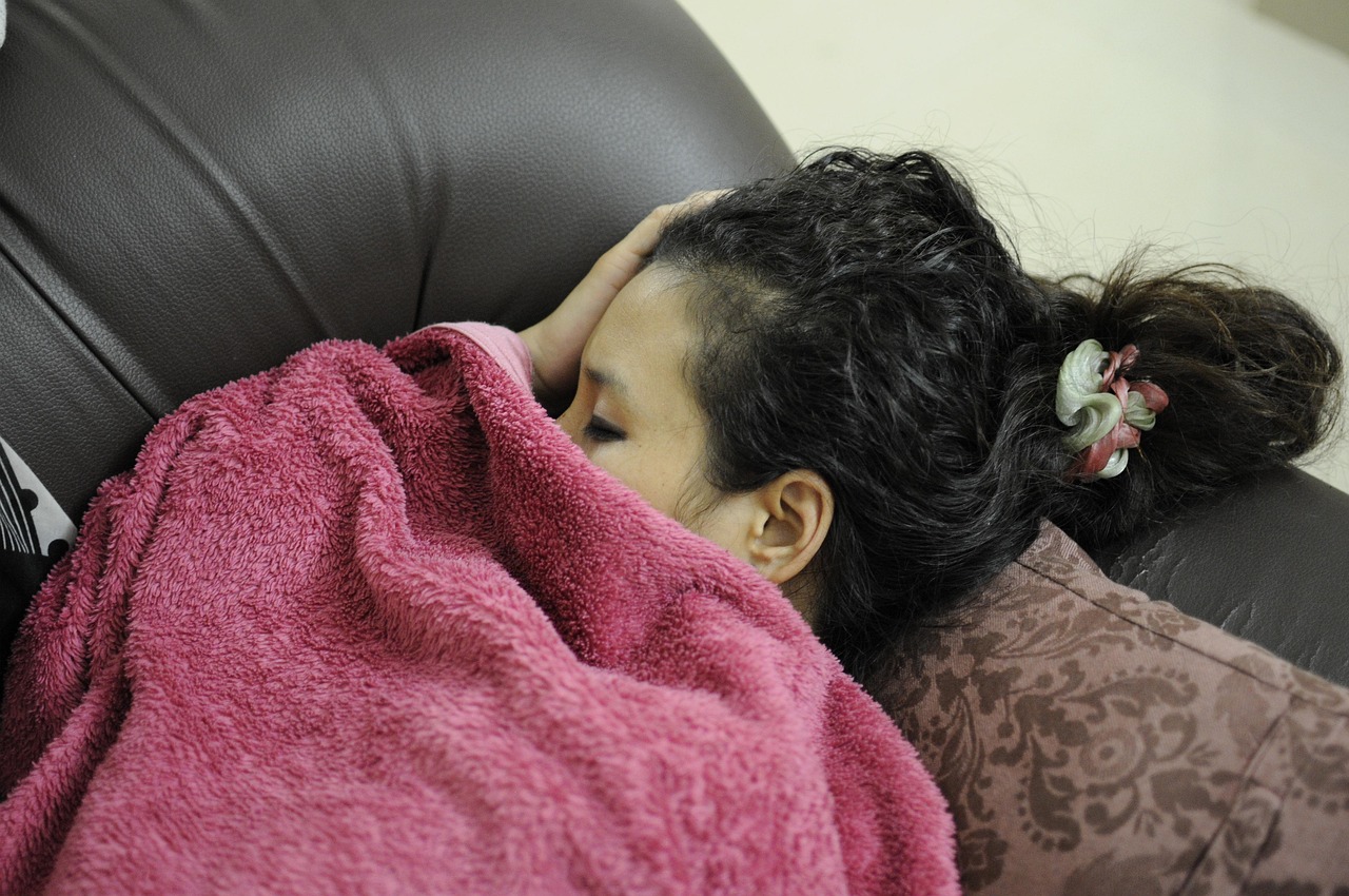 Donna avvolta in una coperta, con espressione di freddo e preoccupazione, in un ambiente domestico.